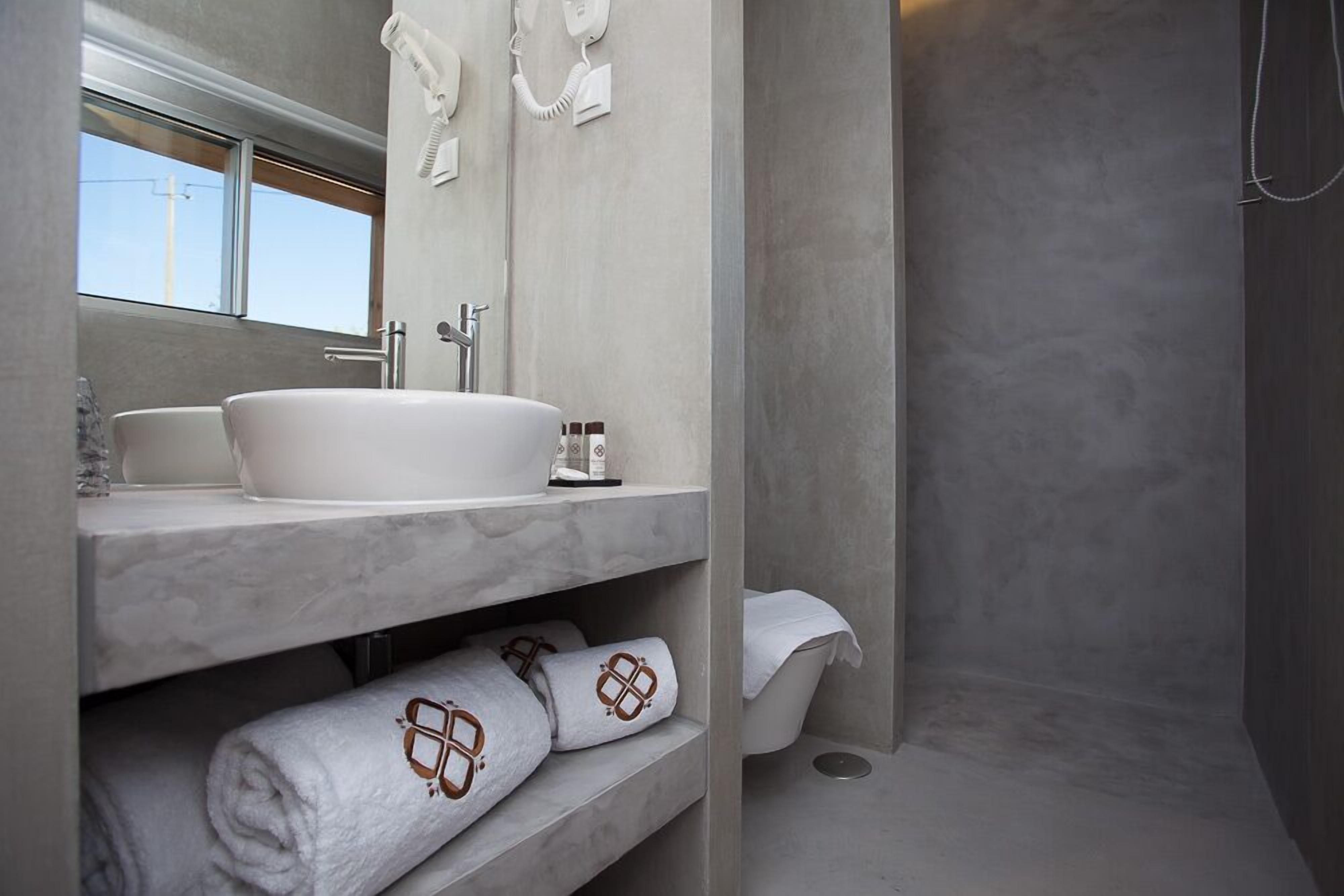 A modern bathroom with a large sink, mirror, and shower. There are towels and toiletries on the shelves.