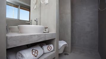 A modern bathroom with a large sink, mirror, and shower. There are towels and toiletries on the shelves.