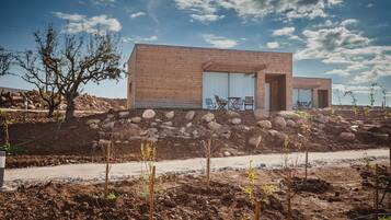 Una casa moderna de dos pisos con fachada de ladrillo, ventanas amplias y un patio con sillas y una mesa.