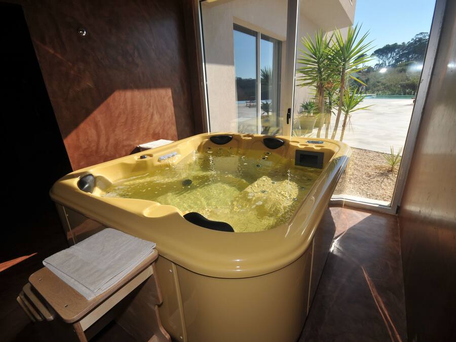 Uma banheira de hidromassagem com um banco de madeira e uma toalha, localizada perto de uma porta de vidro que dá para o exterior.