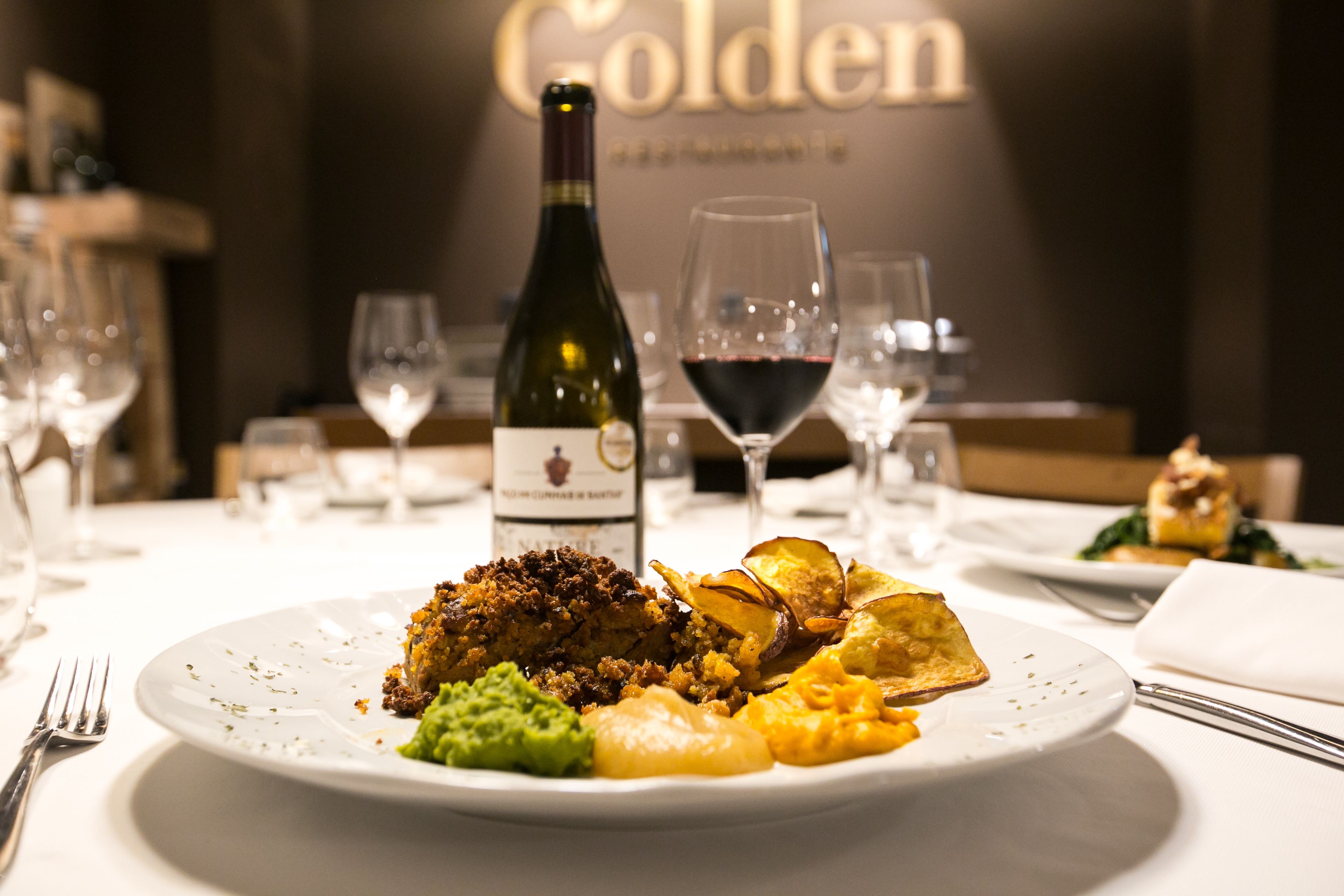A dining table with a plate of food, a bottle of wine, and glasses.