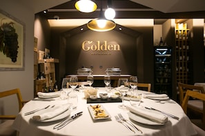 Een restaurantsetting met een gedekte tafel, glazen en een wijnkoeler op de achtergrond.
