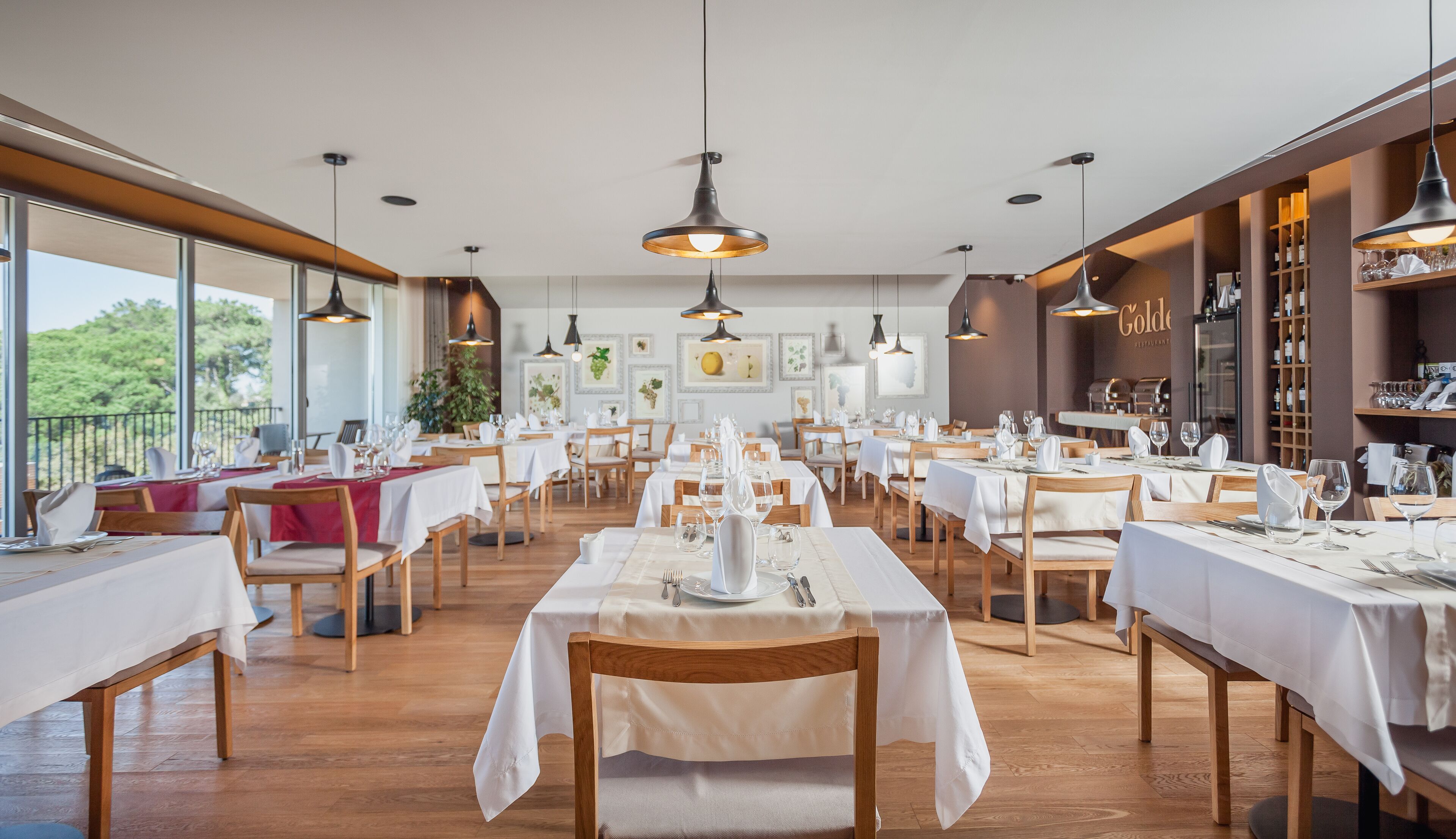 A restaurant with multiple tables set for dining, featuring a modern interior with wooden floors and pendant lighting.