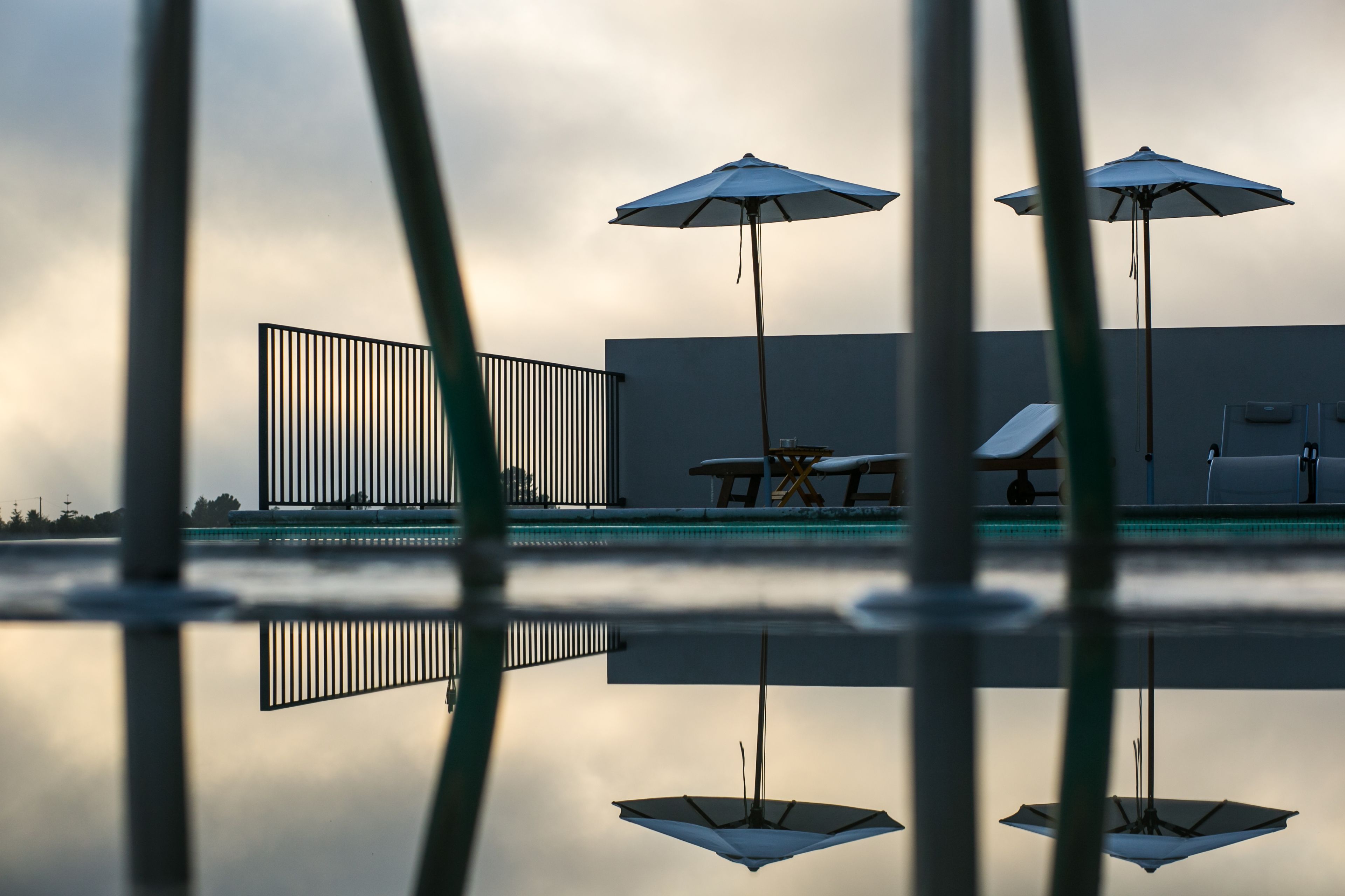 A pool area with umbrellas and lounge chairs, reflecting on the water.