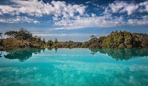 A clear blue pool reflecting trees and a wind turbine in the background. - Vale d'Azenha Hotel and Residences (Alcobaça)