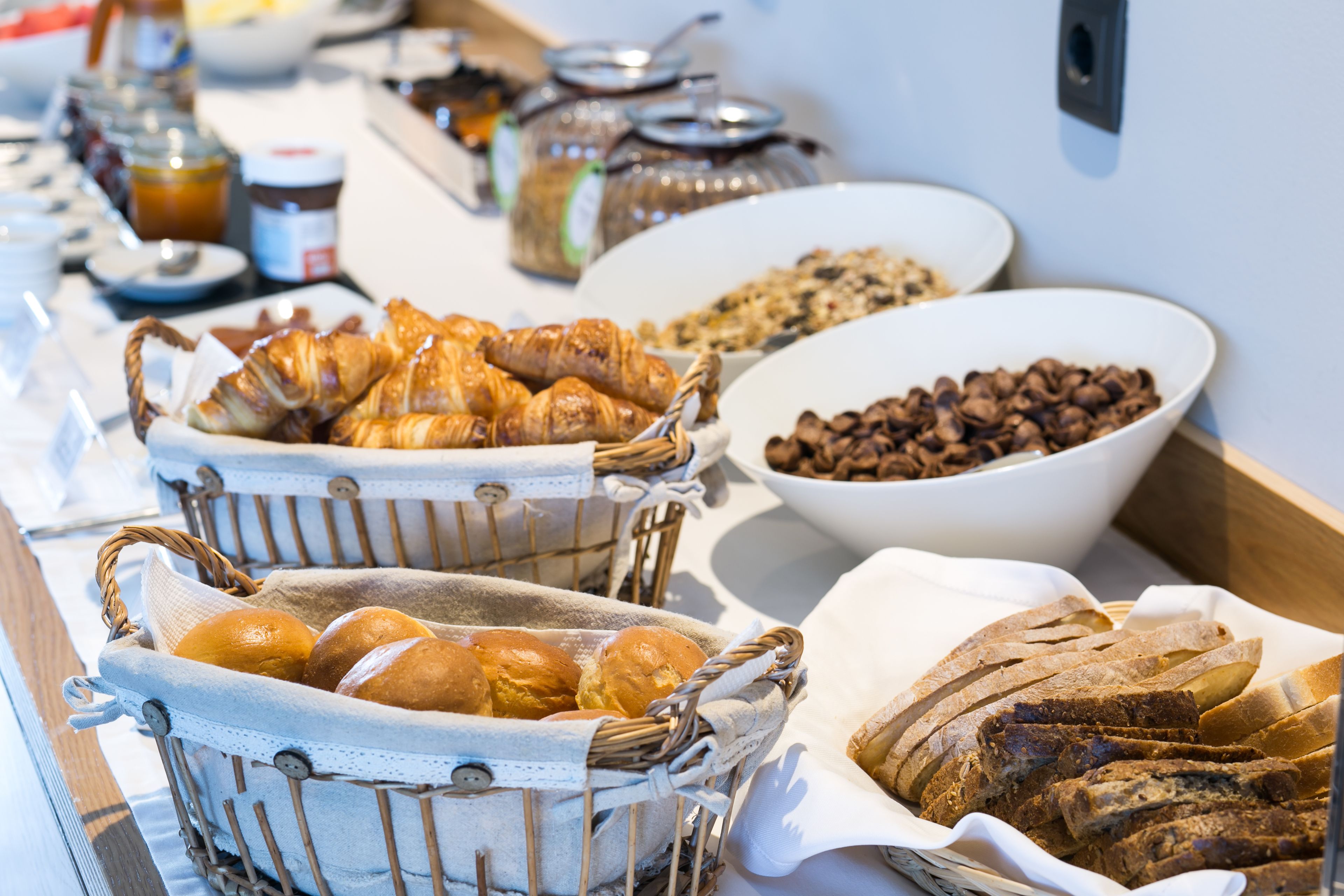 Un bufé con diversas opciones de comida, incluyendo pan, bollería y frutos secos.