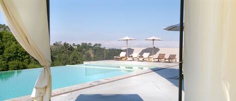 An infinity pool with lounge chairs and umbrellas, overlooking a lush landscape.