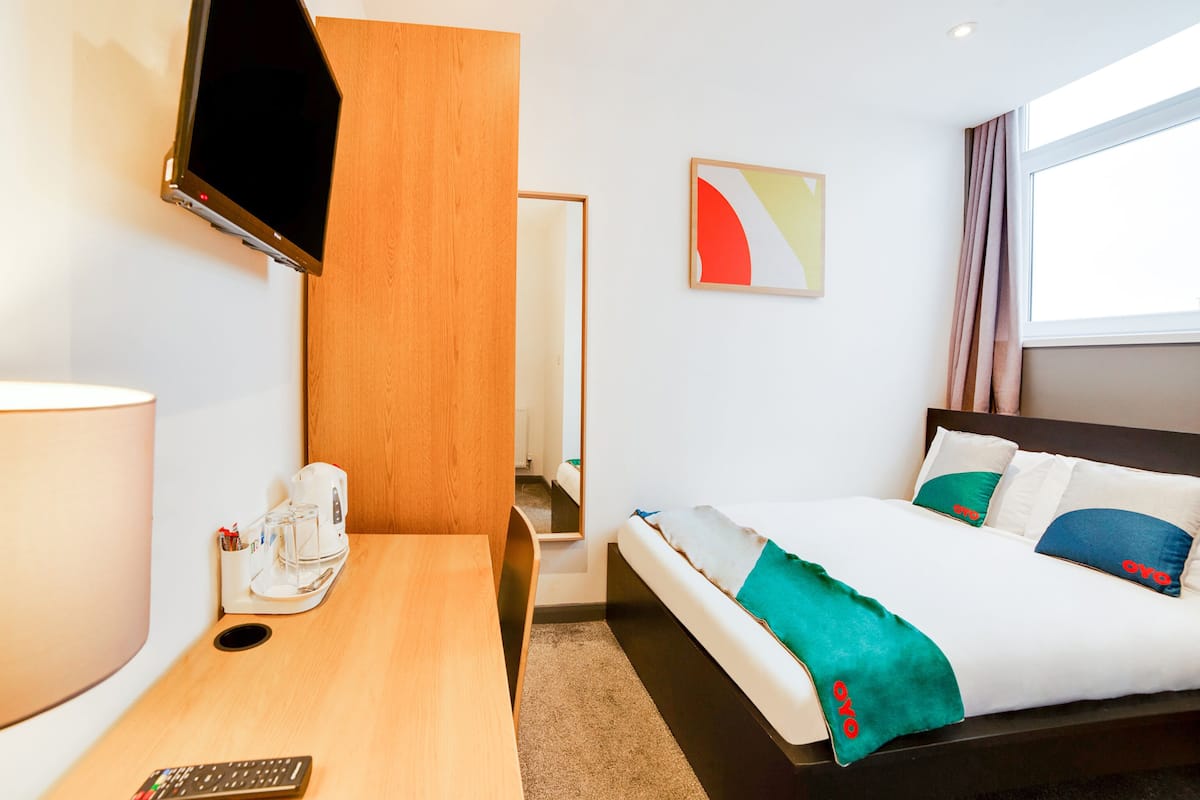 A hotel room with a bed, a desk, a TV, a coffee machine, and a painting on the wall.