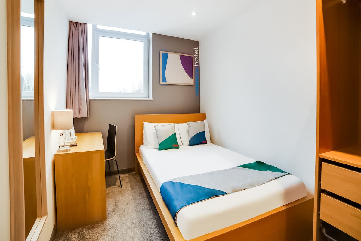 A hotel room with a bed, a desk, a chair, a window, and a wardrobe.