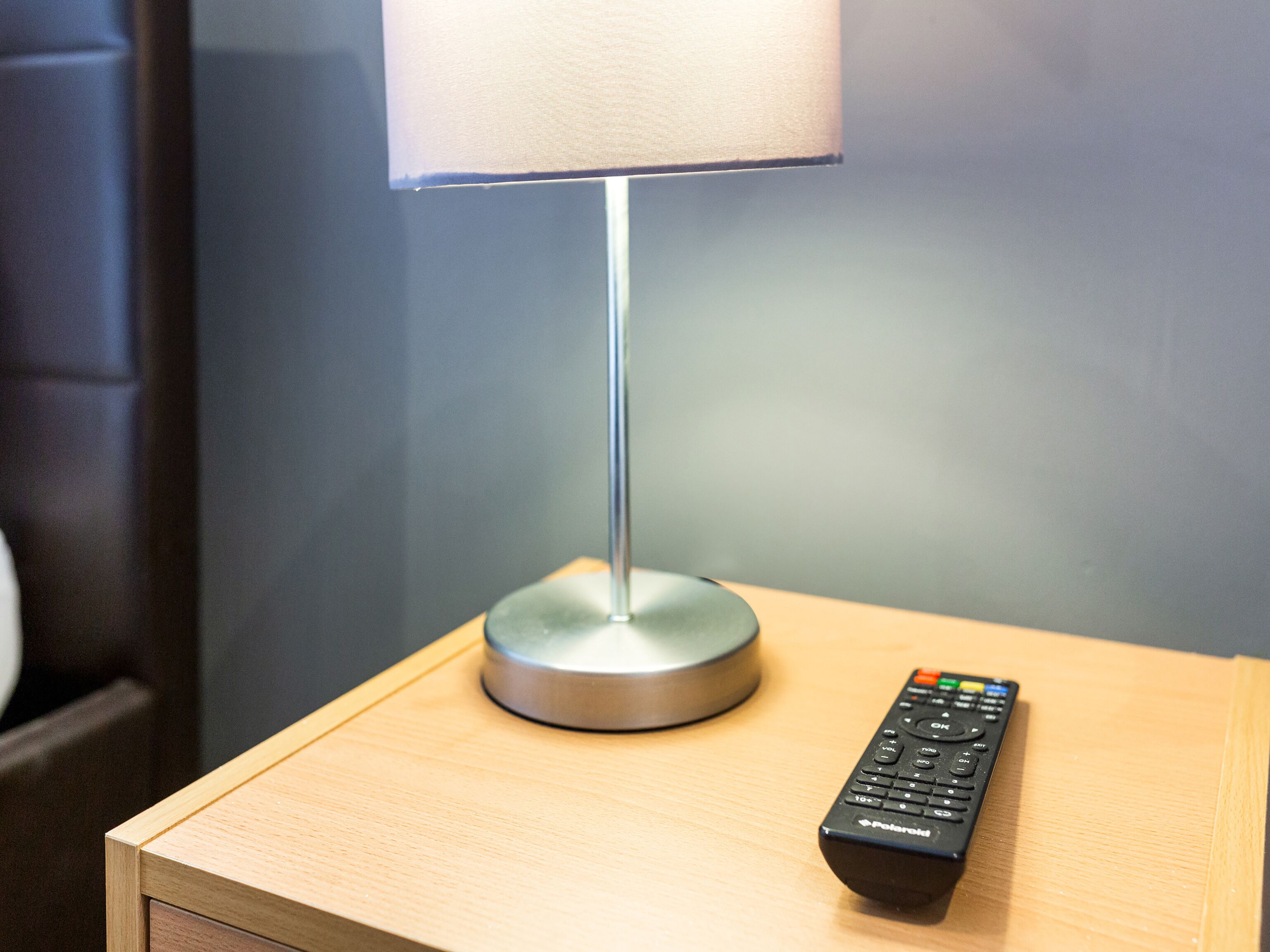 Un comodino in legno con una lampada e un telecomando.