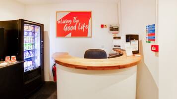 Un área de recepción con mostrador de madera, una máquina expendedora y un cartel en la pared que dice "Living The Good Life".