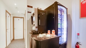 Una máquina de café y un dispensador de bebidas en un pasillo de hotel.