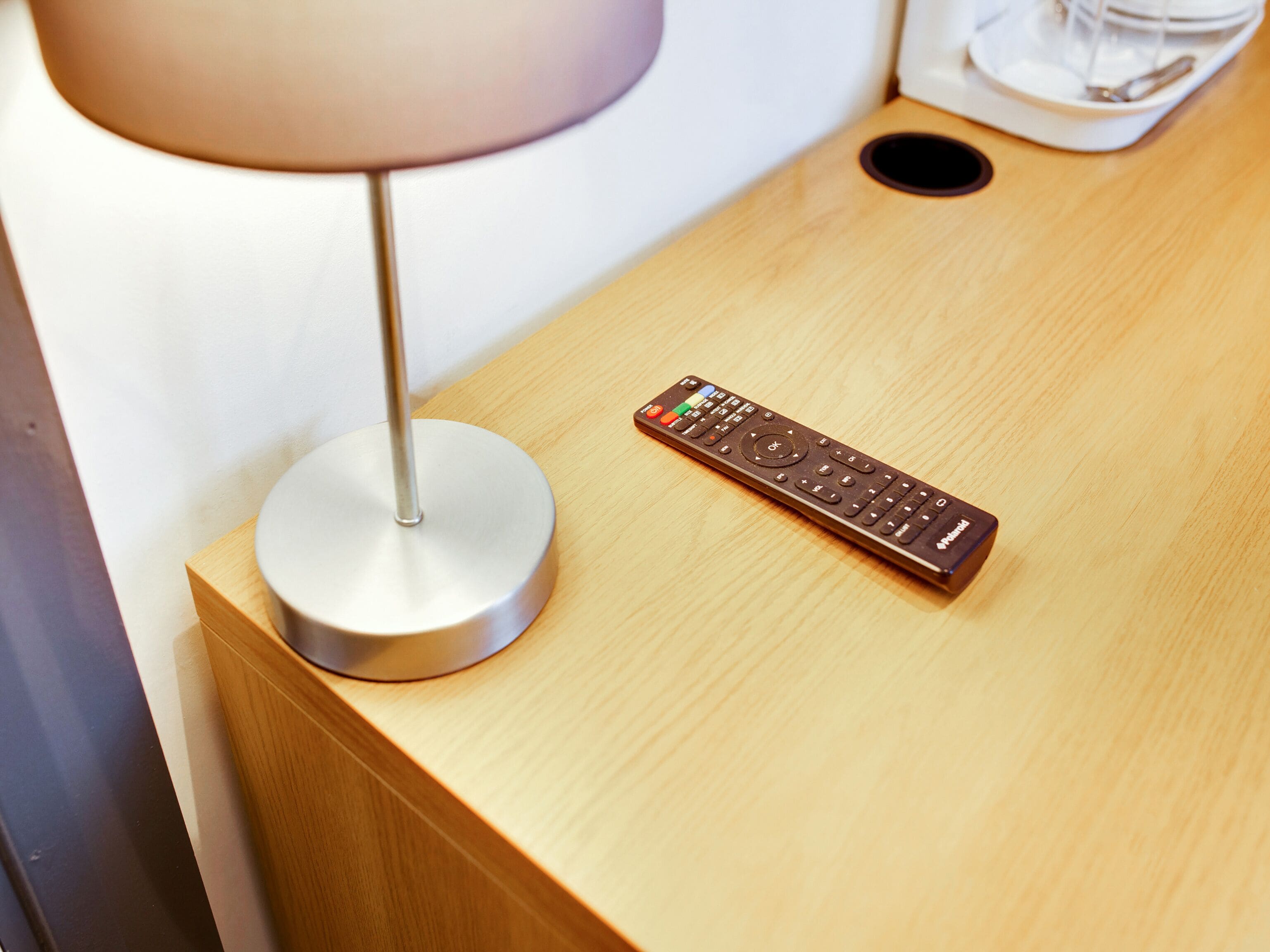 A remote control on a wooden surface next to a lamp.