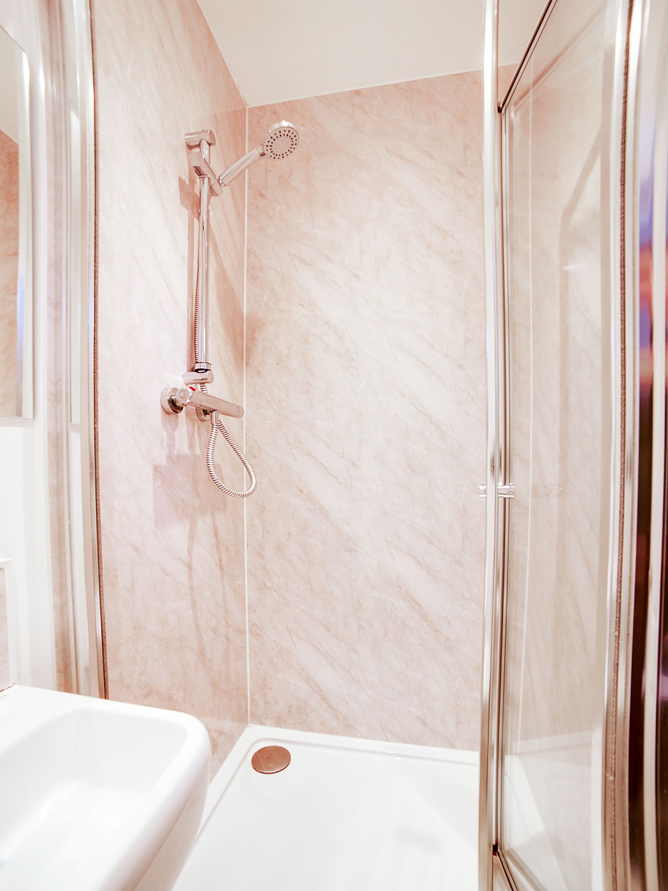A modern bathroom with a glass shower enclosure, a white bathtub, and marble walls.