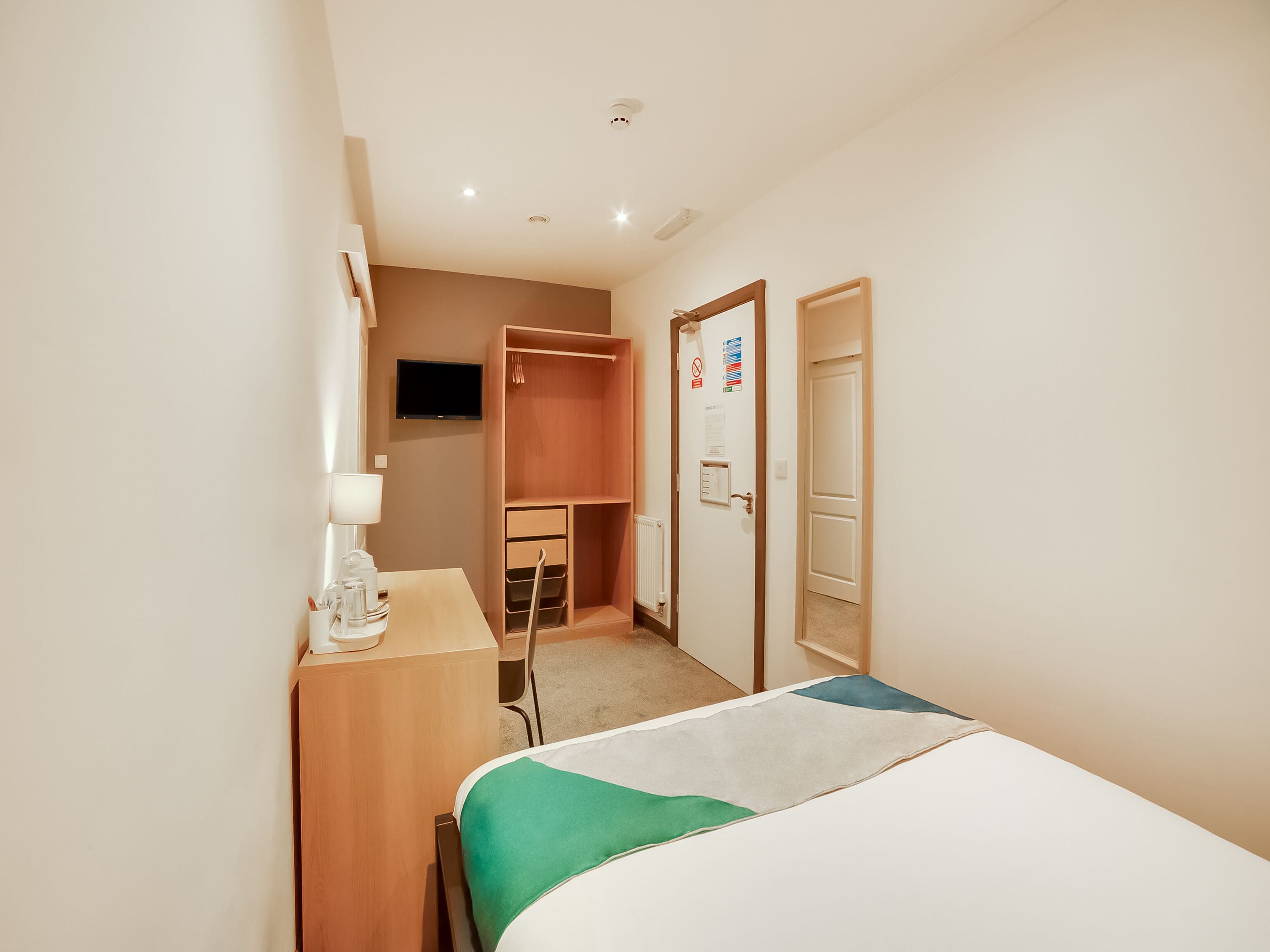 Una habitación de hotel con cama, escritorio con lámpara, armario y puerta con un letrero.