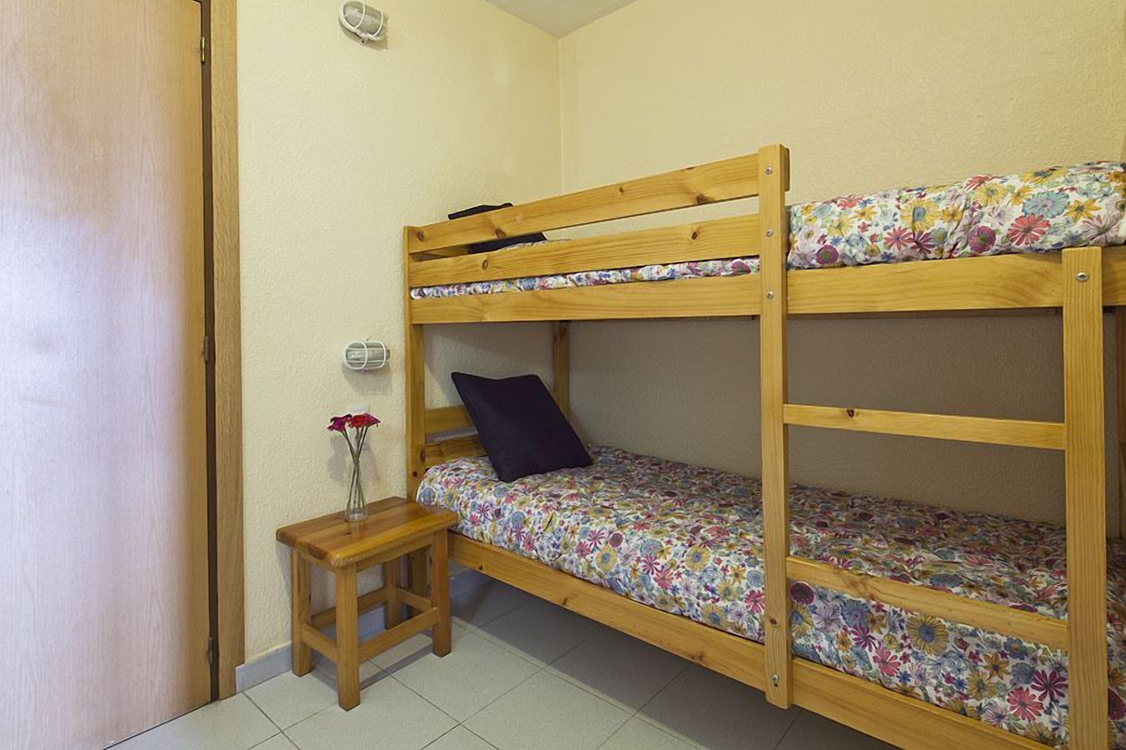 A bunk bed with floral bedding, a small wooden stool, and a vase with flowers.