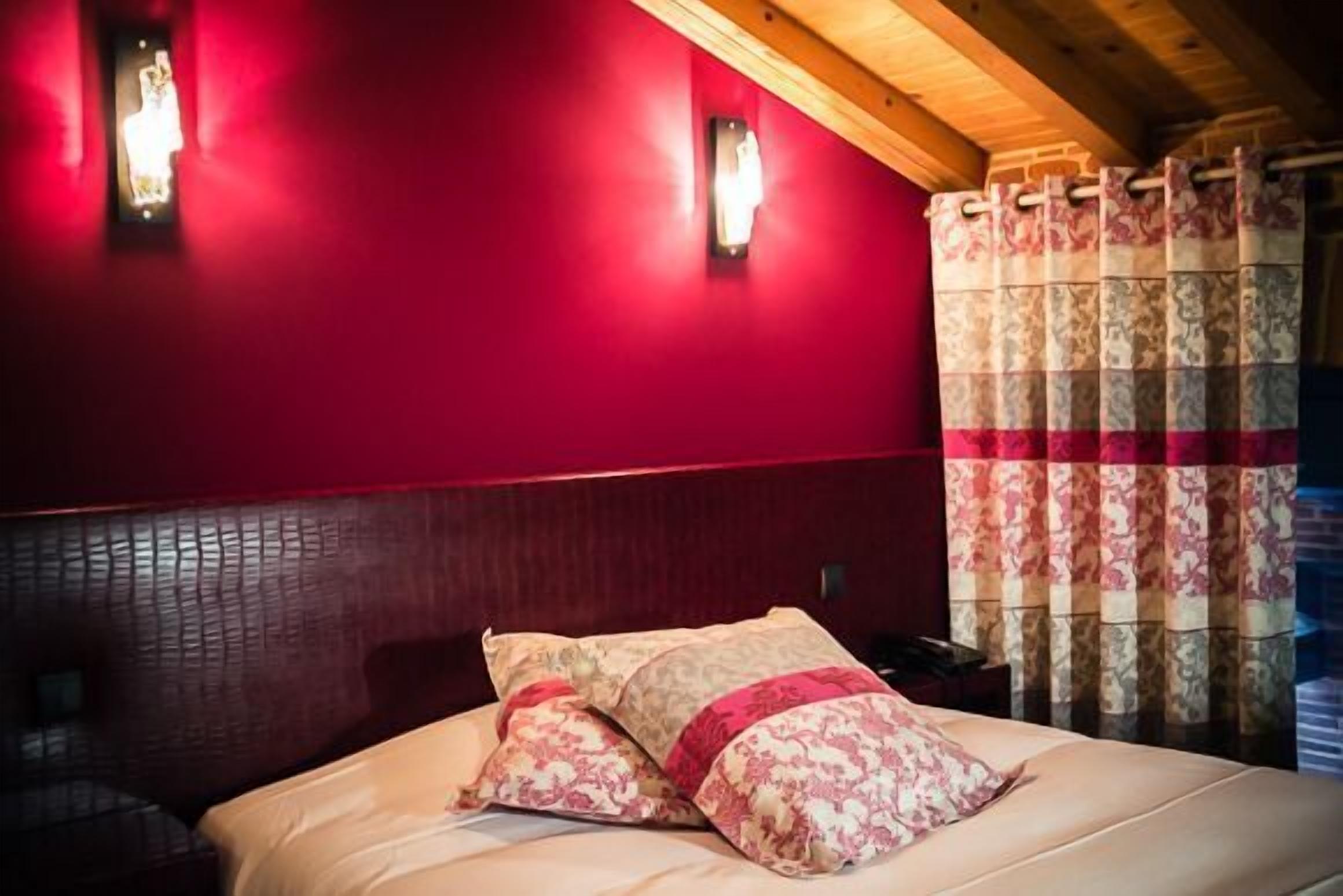A room with a red wall, a wooden ceiling, and a bed with floral bedding.