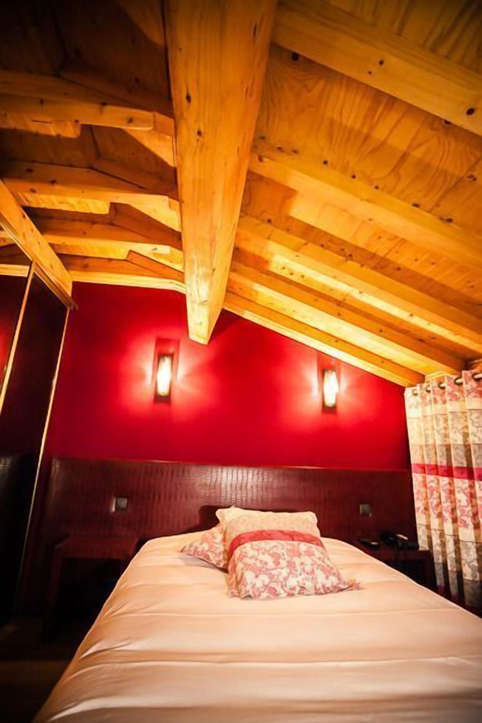 A room with a wooden ceiling, red walls, and a bed with floral bedding.