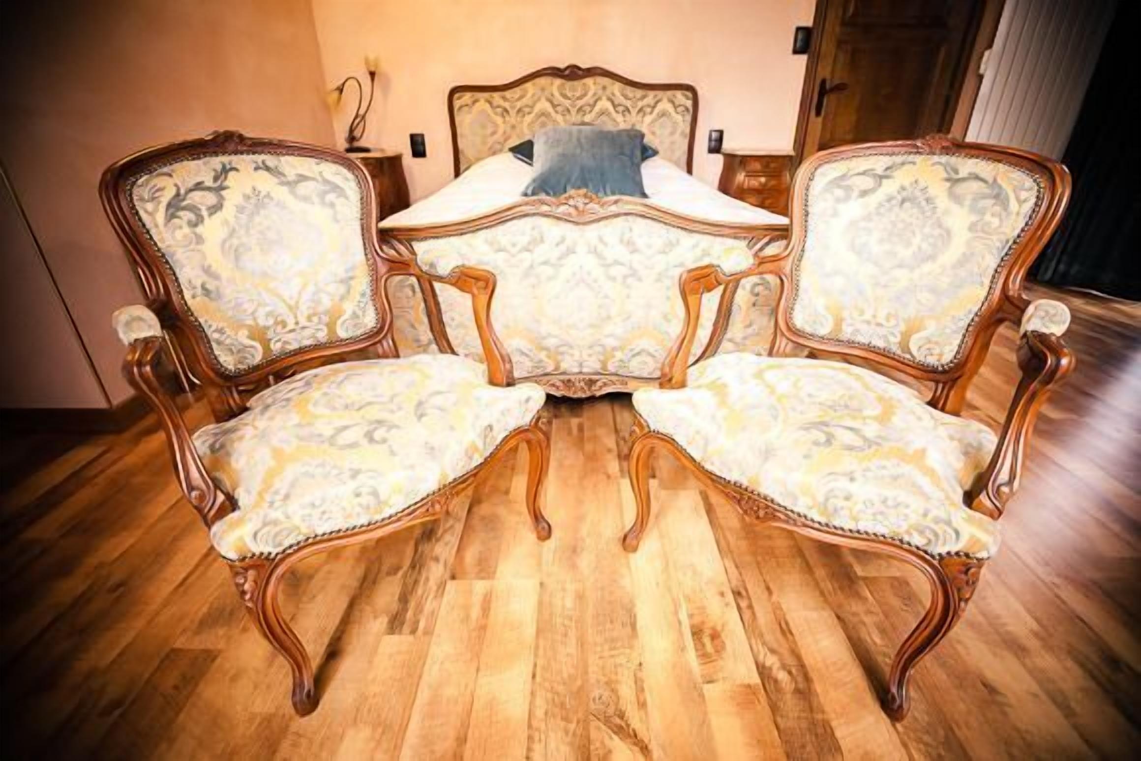Une pièce dotée d’un plancher en bois, d’un lit avec une tête de lit à motifs et de deux fauteuils décoratifs assortis à une table.