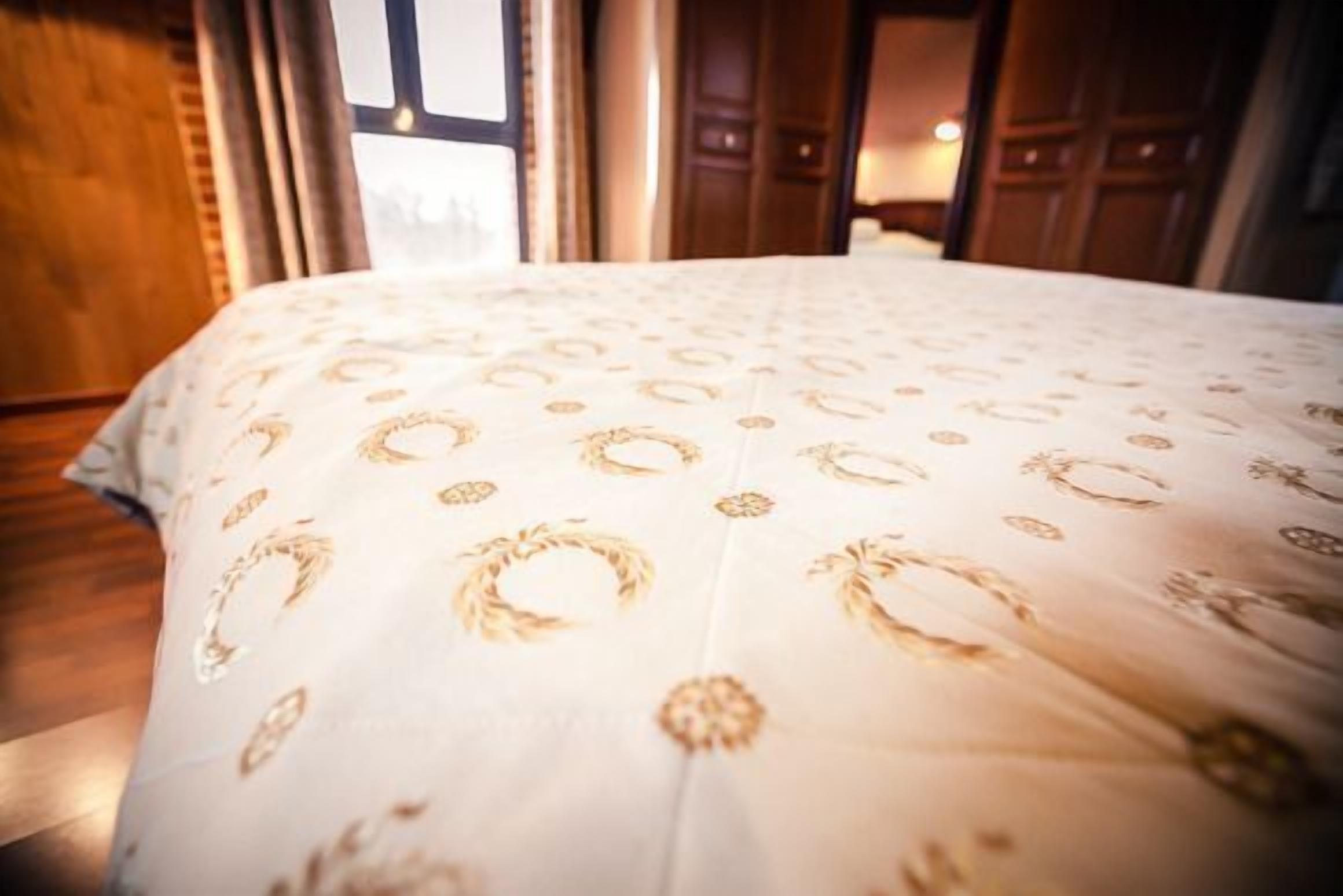 Cama com colcha estampada em quarto com piso de madeira e janela.