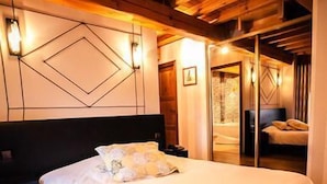A large bed with a wooden headboard, a nightstand, and a wall-mounted light fixture. - Les Ecuries de la Tour (Mondonville)