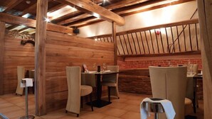 A restaurant with wooden walls and exposed beams, tables with chairs, and a brick wall in the background. - Les Ecuries de la Tour (Mondonville)