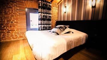 Una camera da letto con parete in mattoni, pavimento in legno, un letto con biancheria bianca e un lampadario fissato alla parete.