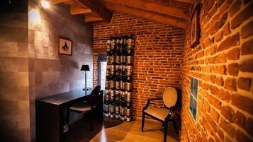 A cozy room with a brick wall, a wooden ceiling, a desk with a chair, and a wine rack.