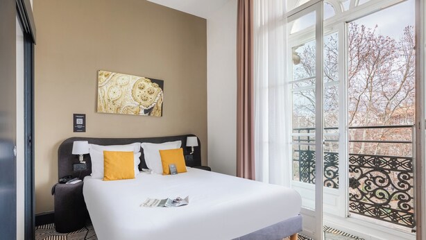 Habitación de hotel con una cama grande, una mesita de noche, una lámpara, una obra de arte enmarcada en la pared y vistas al balcón exterior.