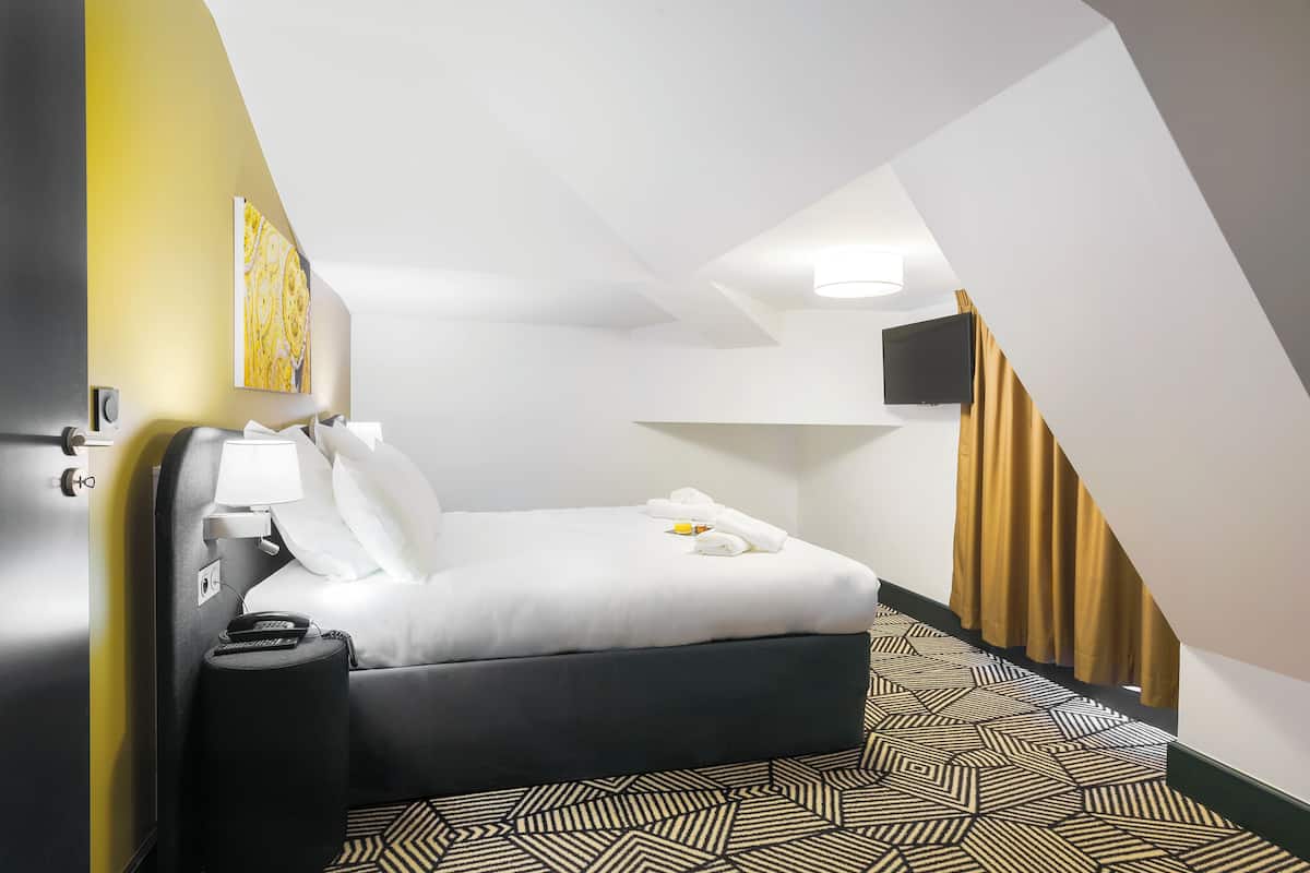 Ein Hotelzimmer mit einem Bett, einem Nachttisch, einer Lampe, einem Fernseher und einem gemusterten Teppich.