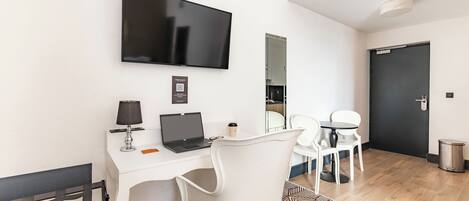 Une chambre d’hôtel moderne avec un bureau blanc, un ordinateur portable, un téléviseur à écran plat, une tasse à café et un tapis à motifs.