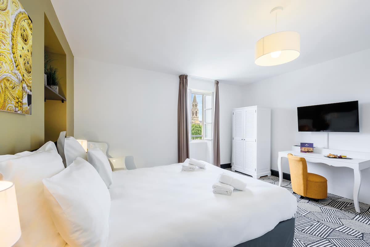 Ein Hotelzimmer mit Bett, Schreibtisch, Stuhl, Fernseher und einem Fenster mit Vorhängen.