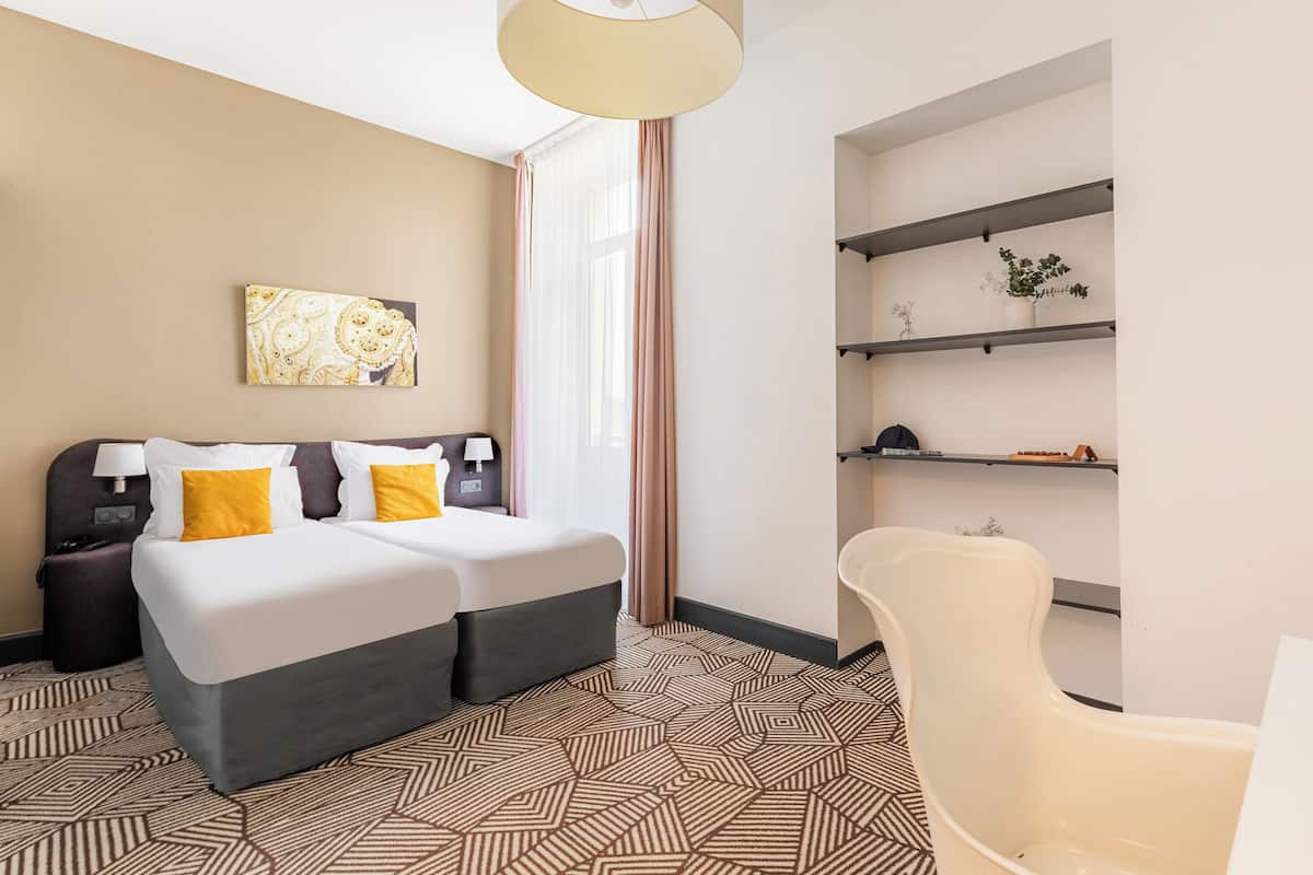Ein Hotelzimmer mit Bett, Nachttischen, einem Sessel, einem Schreibtisch und Regalen mit Pflanzen.