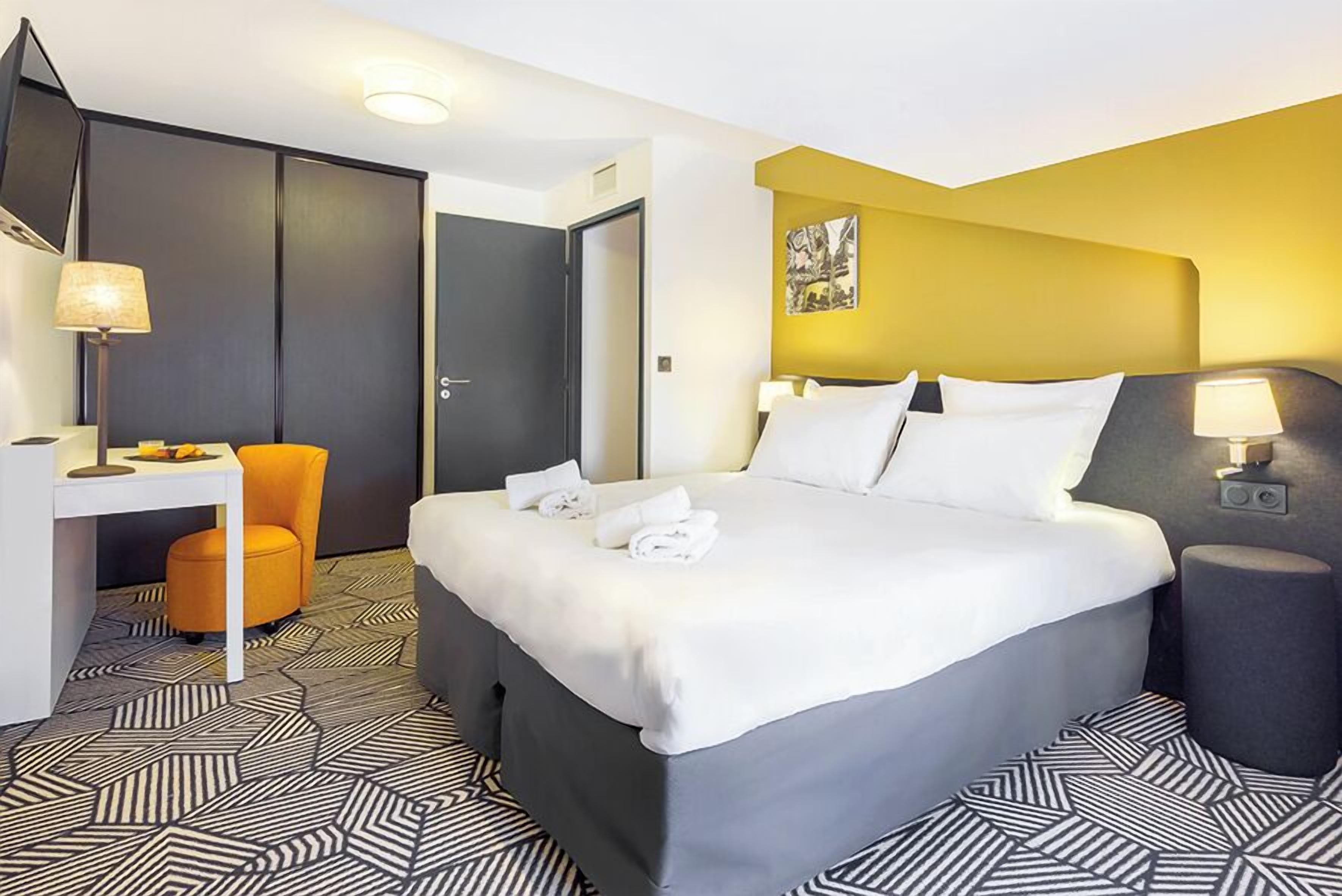 A hotel room with a large bed, a desk, a chair, and a small table.