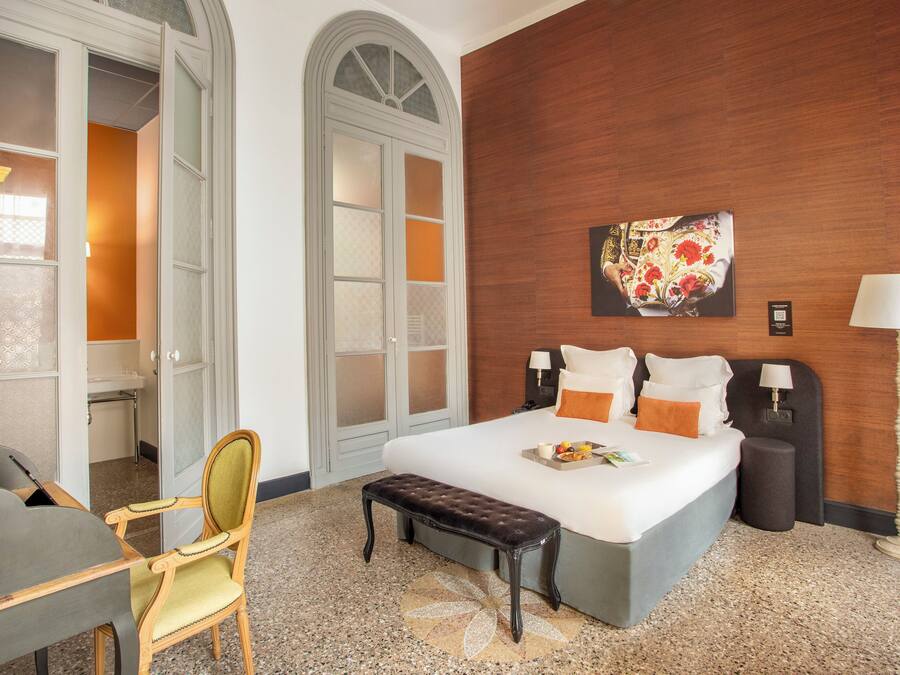 Una habitación de hotel con cama, lámparas de noche, un banco, un escritorio y una silla.