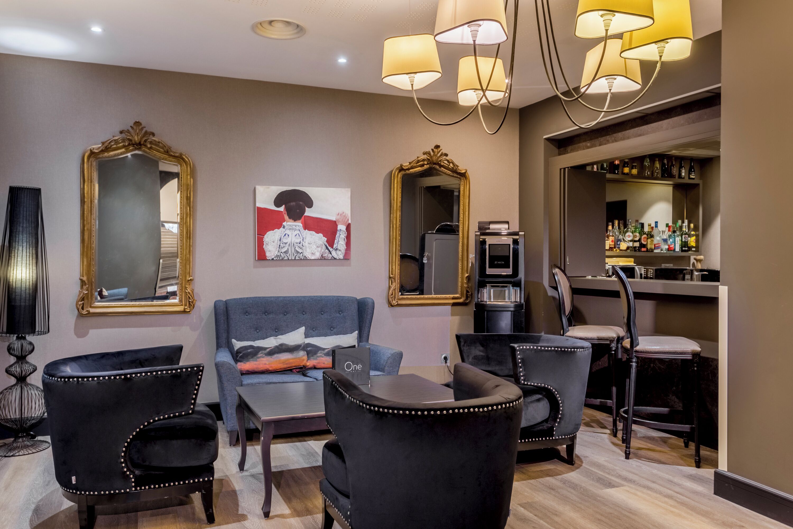 A modern living room with a blue sofa, black armchairs, and a coffee table. There are two large mirrors on the walls, a painting, and a bar area with bottles.
