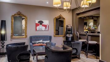 A modern living room with a blue sofa, black armchairs, and a coffee table. There are two large mirrors on the walls, a painting, and a bar area with bottles.
