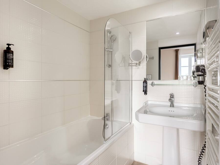 Un baño moderno con ducha de vidrio, lavamanos blanco y espejo sobre él.