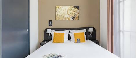 Habitación de hotel con cama, dos mesitas de noche, un aparador, una obra de arte en la pared y una ventana con cortinas.