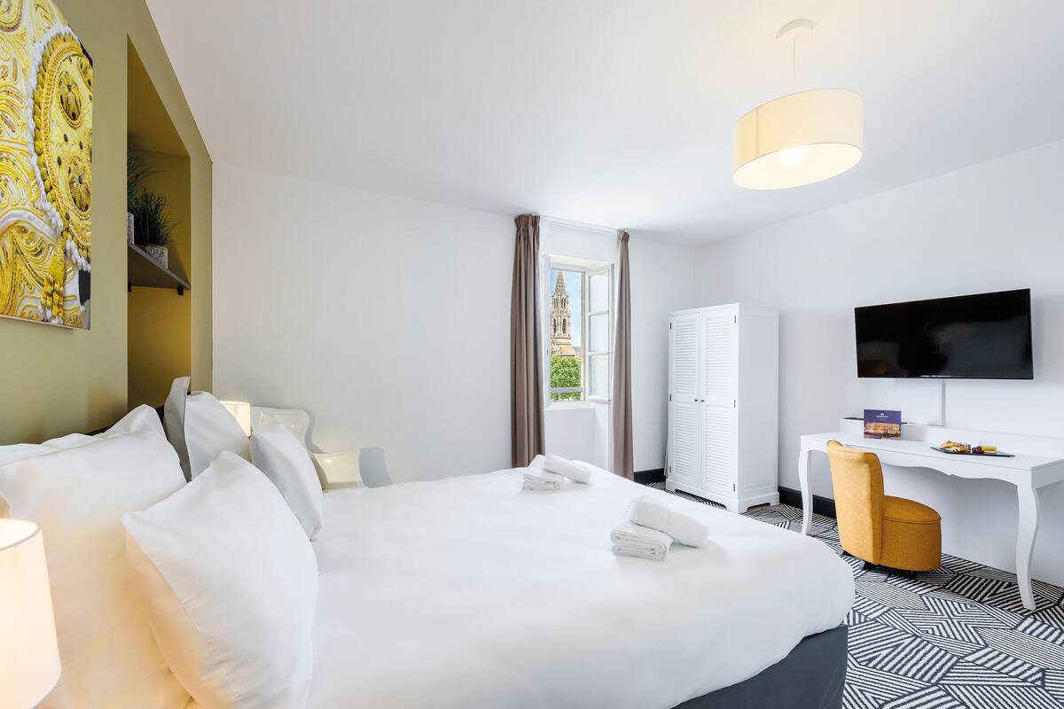 Ein Hotelzimmer mit Bett, Schreibtisch, Stuhl, Fernseher und einem Fenster mit Vorhängen.