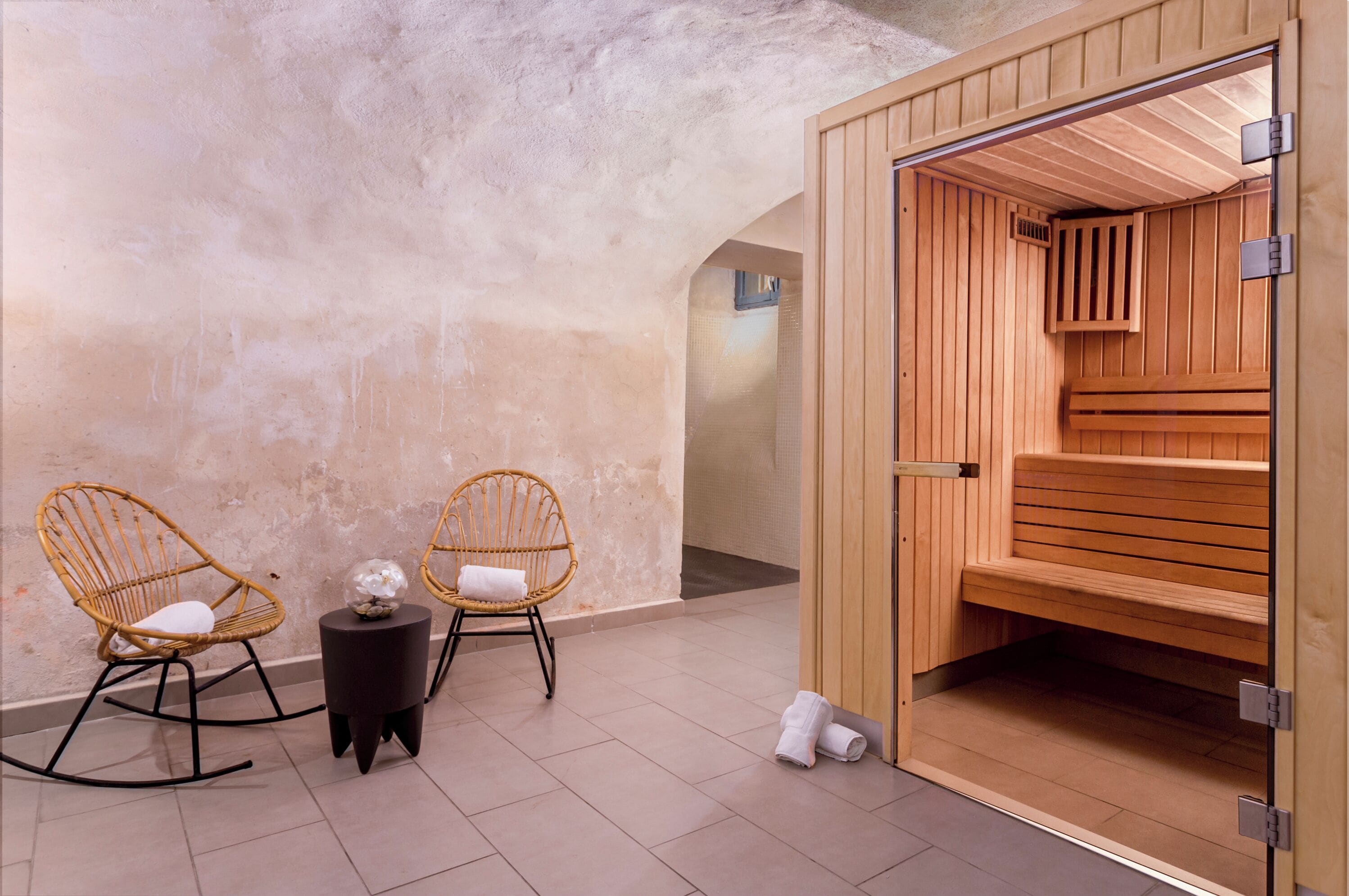 A spa room with two wicker chairs, a small table with a decorative item, and a wooden sauna.