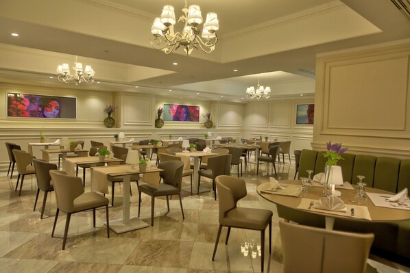 Un comedor de hotel con varias mesas y sillas, candelabros y televisores montados en la pared.