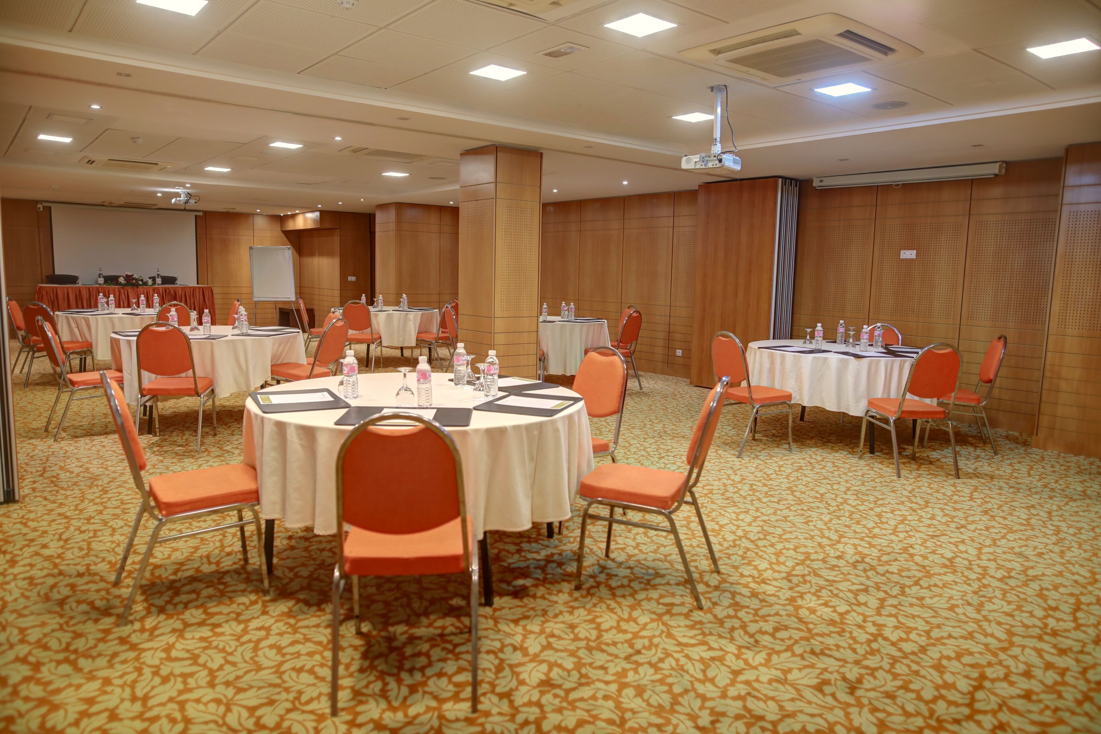Une salle de conférence avec des tables rondes, des chaises orange et un sol recouvert de moquette.