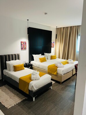 Hotellihuone, jossa on kaksi sänkyä, musta pääty, suuri ikkuna verhoilla ja taideteoksia seinillä.