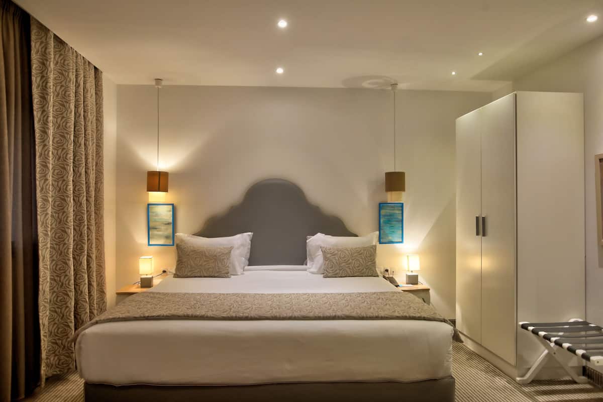 A hotel room with a large bed, bedside tables with lamps, a wardrobe, and a headboard with a unique design.