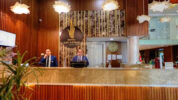 A hotel reception desk with a wooden panel design, a clock, and a sign indicating the hotel name.