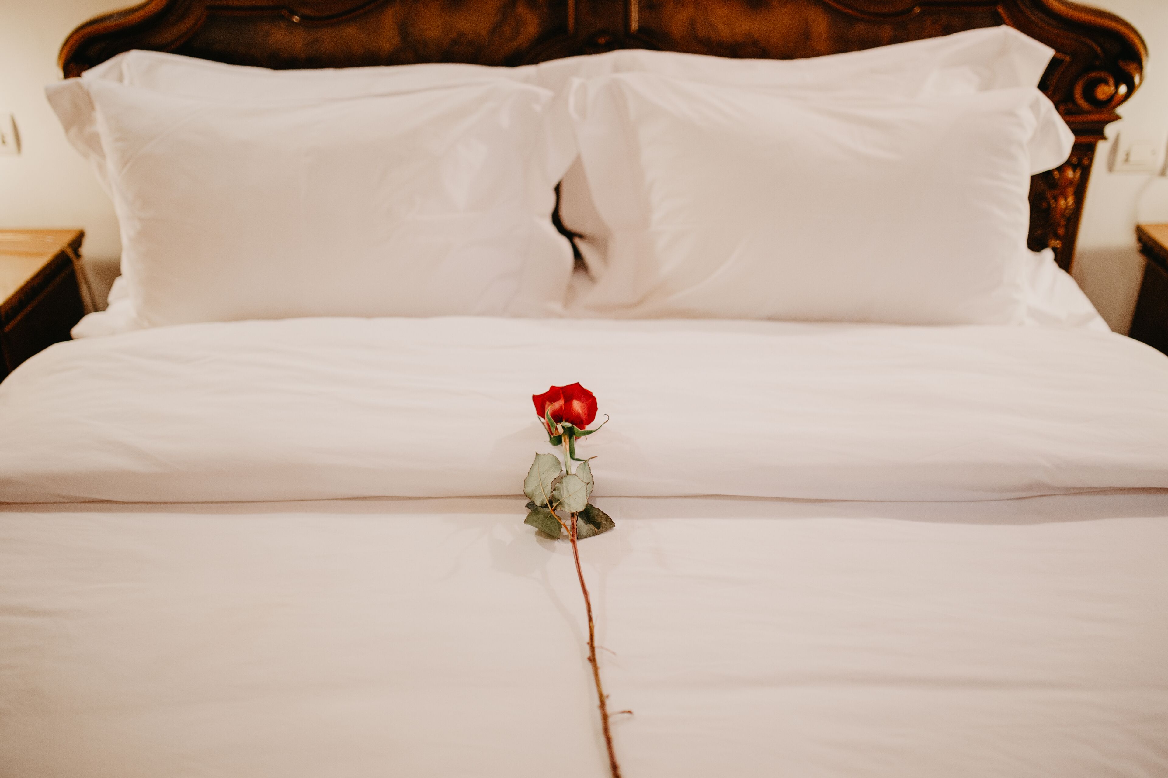 Cama com lençóis brancos e uma única rosa vermelha colocada no centro.