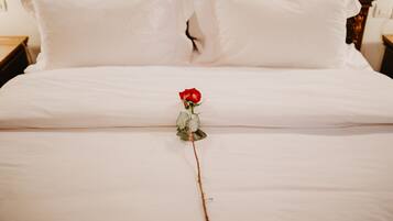 Cama com lençóis brancos e uma única rosa vermelha colocada no centro.