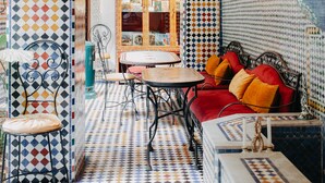 A room with patterned tile flooring, a red sofa with orange cushions, a small table, and a chair. - Riad TOYOUR (Fes)