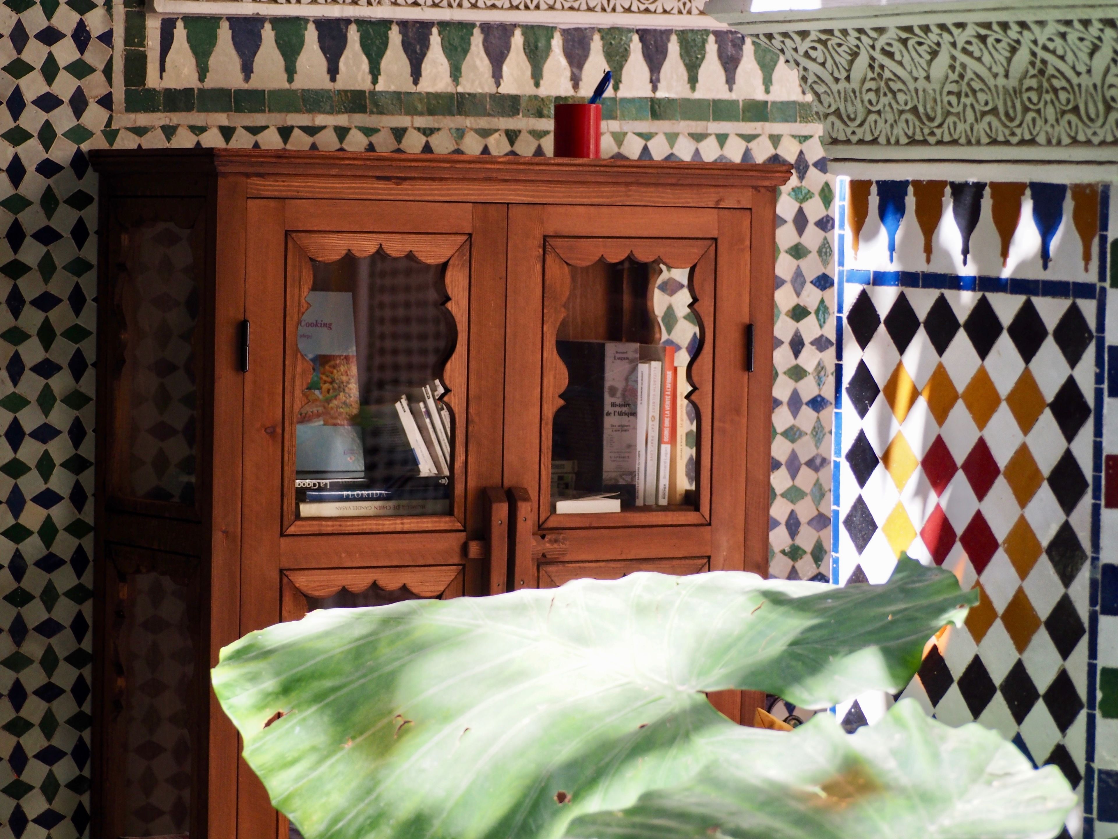 A wooden cabinet with glass doors, a red cup on top, and a patterned wall.